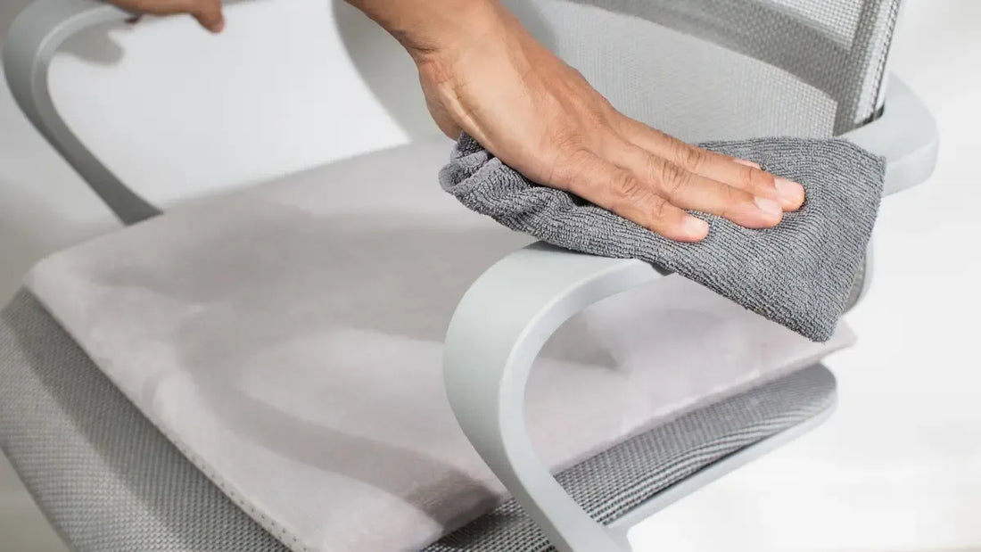 Technician wiping down a used mesh ergonomic office chair with a microfiber cloth before sale